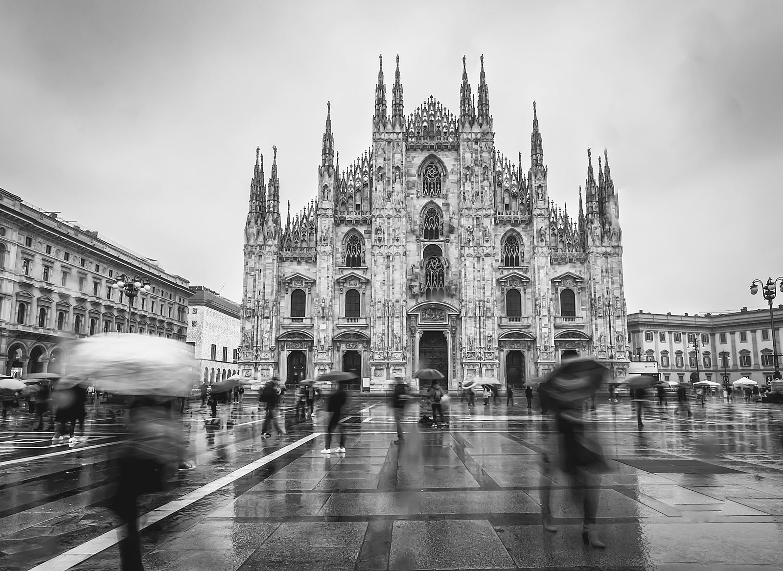 Piazza del Duomo a Milano sotto la pioggia, in bianco e nero, con passanti e ombrelli in movimento davanti alla cattedrale